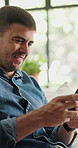 Smile, man and reading with phone at house for games, browsing website and networking. Happy, male person and mobile app on couch for streaming movies, social media and notification of message update