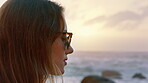 Sunset, thinking and woman with sunglasses by ocean, remember sad memory and introspection for holiday. Beach, summer break and calm person with disappointment for vacation, shades or past reflection
