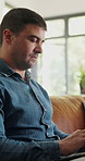 Typing, laptop and man in home for remote work, editing article or reading blog on sofa. Computer, living room and freelance copywriter in house, check story and review newsletter with research