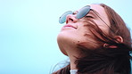 Breathing, sunglasses and windy with woman outdoor for adventure hike, fresh air or solitude. Breeze, space and thinking with happy person on blue sky for hiking holiday, vacation or weekend morning