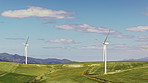 Wind turbine, grass field and clouds with blue sky for renewable energy or economic development. Windmill, sustainability or eco friendly environment with natural resource or power in countryside