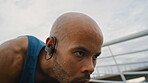 Man, sweating and start running in city with earphones, intense exercise or endurance training outdoor. Active, person and runner breathing on bridge with audio tech, begin sprint and cardio workout.