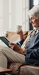Coffee, tablet and senior woman in living room for reading news, relax or email in retirement home. Warm beverage, technology and elderly person on sofa for online article, ebook or rest on weekend