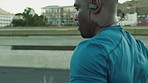 Black man, running and earphones on bridge for fitness in city for cardio, training and wellness in summer. African person, outdoor and fast with music, workout and streaming service in urban town