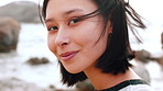 Wellness, face or Asian woman at seaside with wind, positive attitude or chill on weekend break. Peaceful, portrait or person at beach with fresh air, good mood or outdoor getaway in New Zealand.