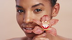 Woman, orchid and face for skincare in studio with flower, beauty or natural glow on background. Girl, happy and floral blossom with sustainable cosmetics, confident and pride with wellness in Brazil