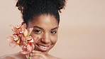 Face, skincare and black woman with flower, organic cosmetic or antioxidants for antiaging benefits. Happy, female person and orchid plant for dermatology, wellness or self care on studio background.