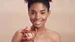 Face, skincare and woman with orchid plant, organic cosmetic or antioxidants for antiaging benefits. Happy, black person and pink flower for dermatology, beauty or body wellness on studio background.