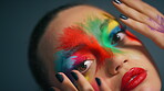 Face, art and woman with rainbow makeup, studio background or beauty aesthetic with colorful fantasy. Serious, person and self expression with red lipstick, paint and creative with cosmetics and glow