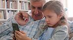 Grandpa, phone and talking with girl on sofa in home living room for bonding, learning or visit. App, gaming and streaming with happy senior man teaching grandchild in apartment for mobile connection