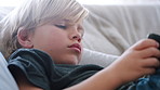 Gaming, phone and relax with boy on sofa in living room of home for morning or weekend streaming. App, development and mobile video game with child in apartment for digital or online subscription