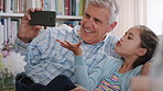 Grandpa, greeting and video call with girl on sofa in home living room for bonding, love or visit. App, blowing kiss and wave of senior man with happy granddaughter in apartment for communication