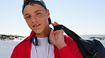 Face, student and teen with headphones at beach, outdoor and confident with high school scholarship. Ocean, commute and boy with bag in nature, education and smile for study opportunity in Canada