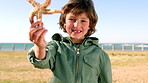 Boy, face and happy at beach for starfish on promenade in summer, vacation or learning in nature. Child, smile and portrait with invertebrate, marine animal or seaside holiday on lawn in New Zealand