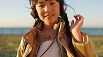 Travel, face and child with headphones at beach, happy and listening to music on getaway or outdoor. Ocean, vacation and girl with tech for audio, streaming and song subscription in nature and break