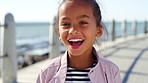 Face, funny and girl at promenade, kid and summer holiday to relax, travel weekend and humor. Ocean, youth or child with break, sunshine or laughing with vacation, adventure or getaway trip in Bali