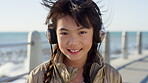 Outdoor, face and child with headphones at beach, relax and listening to music on holiday or getaway. Ocean, vacation and girl with tech for audio, happiness and streaming song in nature and travel