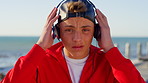 Boy, teenager and face at beach with headphones on holiday with fashion, ocean and serious in summer. Child, audio and cap for portrait on boardwalk with streaming, music or seaside vacation in Spain