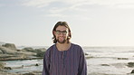 Happy, travel and face of man on beach for holiday, adventure and tourism for summer vacation. Nature, smile and portrait of person by ocean, sea and outdoor for fresh air, peace and wellness