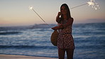 Woman, dance and sparklers at beach with smile on vacation, space and outdoor in evening on ocean getaway. Girl, excited and happy with fireworks, dusk and party with celebration on seaside holiday