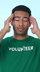 Volunteer, pain and man in studio with headache for charity work, outreach program and community service. Fatigue, migraine and person with stress for ngo, nonprofit and donation on blue background