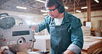 Carpentry, earmuffs and sawing machine with man in warehouse for manufacturing or production process. Bandsaw, eyewear and ppe with person in woodworking plant to resize lumber or timber for project