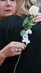 Old woman, hug and flowers at cemetery for funeral procession, mourning and loss at ceremony. People, family and white rose with grief, support or respect with embrace for memorial at graveyard