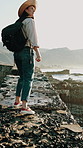 Rocks, walking and back of woman by ocean for travel, adventure and backpacking in nature. Tourism, morning and person by seaside pier for sightseeing on holiday, vacation and weekend in Australia