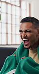 Celebration, flag of Brazil and shouting with excited man on sofa as soccer or sports fan. Achievement, cheering and streaming with football supporter in home living room for success or victory