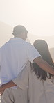 Couple, hug and walking by ocean with summer holiday, sunshine and connection for bonding together. Back, married people and embrace on beach with love, tropical vacation and holding hands for trust.