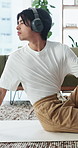 Man, headphones and stretching in home with yoga, wellness and listening to music for mindfulness. Zen, Asian person and spinal twist on floor with flexibility, holistic health and tech for audio.