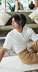 Man, headphones and stretching in house with yoga, wellness and listening to music for mindfulness. Zen, Asian person and spinal twist on floor with flexibility, holistic health and tech for audio.