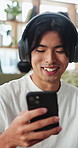 Man, laugh and headphones in home with phone, funny social media video and text message notification. Happy, Asian person and scroll in living room with audio tech, online meme and podcast humor.