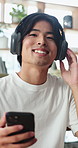 Happy, man and headphones in living room with phone, relax and listening to favorite music in house. Asian person, click tech and smile in apartment with wellness, streaming audio and online radio.