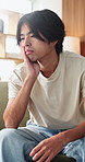 Sad, thinking and man in home, anxiety and mental health with loss, lonely and wonder. Apartment, depression and Asian person in lounge, contemplation and reflection for nostalgia, grief and remember