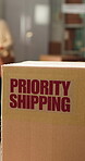 Logistics, box and priority shipping label in office, package distribution and express order delivery. Space, supply chain and parcel with courier sticker to streamline transport, startup and people