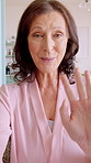 Face, wave and mature woman on video call, talking and  communication with contact in house. Portrait, virtual chat and happy person with hand gesture for welcome, greeting or hello with POV in home