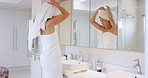 Bathroom, woman and towel for hair care in home with shampoo, conditioner, and reflection in mirror. Female person, washing and house with maintenance for hygiene, grooming and wellness in morning