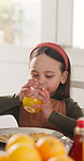 Breakfast, kid and drink orange juice in home for diet, wellness and hydration in dining room. Morning, thirsty girl and fruit beverage for nutrition, growth and development with energy in house