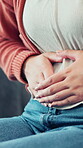 Hands, pain and woman with stomach ache on sofa for menstruation, discomfort and PMS crisis. Endometriosis cramps, person and belly indigestion in home from ovulation cycle, IBS or abdominal bloating