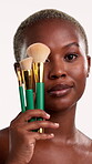 Face, makeup and black woman with brushes in studio, facial beauty routine and makeover aesthetic. Portrait, smile and person with application tools for cosmetics, confident and white background 