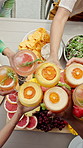 People, hands or fruit with cheers above for healthy dinner, social gathering or breakfast together. Top view, group or friends with cocktail glasses or food for toast, dining or event at table