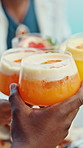 People, hands and glasses with cheers for dining, social gathering or event together. Happy, group or friends with cocktail, fruit or food for toast, celebration or tropical party at dinner table