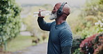 Fitness, headphones and old man drinking water at park for running break, hydration or electrolyte. Active, retirement or senior black person with liquid for workout nutrition, thirst or cardio audio