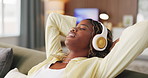 Black woman, relax and listening with headphones on sofa for music or audio streaming in home. Female person, comfort or smile with break or rest for podcast, sound therapy or stress relief in house