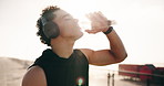 Man, fitness and drinking with water bottle on promenade for outdoor workout, break or recovery. Active, male person or sun with mineral liquid or headphones for exercise, rest or training in nature