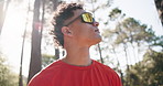 Fitness, thinking and man in woods, low angle and breathing with break, exercise and wellness. Sunshine, rest or person with pause, workout for health benefits or challenge with contemplation or calm