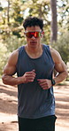 Man, fitness and running with sunglasses in forest for outdoor workout, exercise or training. Active, male person or runner with wristwatch for monitoring or tracking performance in nature or woods