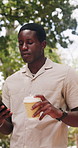 Walking, coffee and black man in park, phone for social media and online reading. Outdoor, mobile user and African person with herbal tea, tech for texting and message to contact, typing and internet