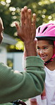High five, father and girl with helmet in backyard, safety practice and support for cycling lesson. Smile, protection gear and man with child to learn responsibility, getting ready and bokeh by home